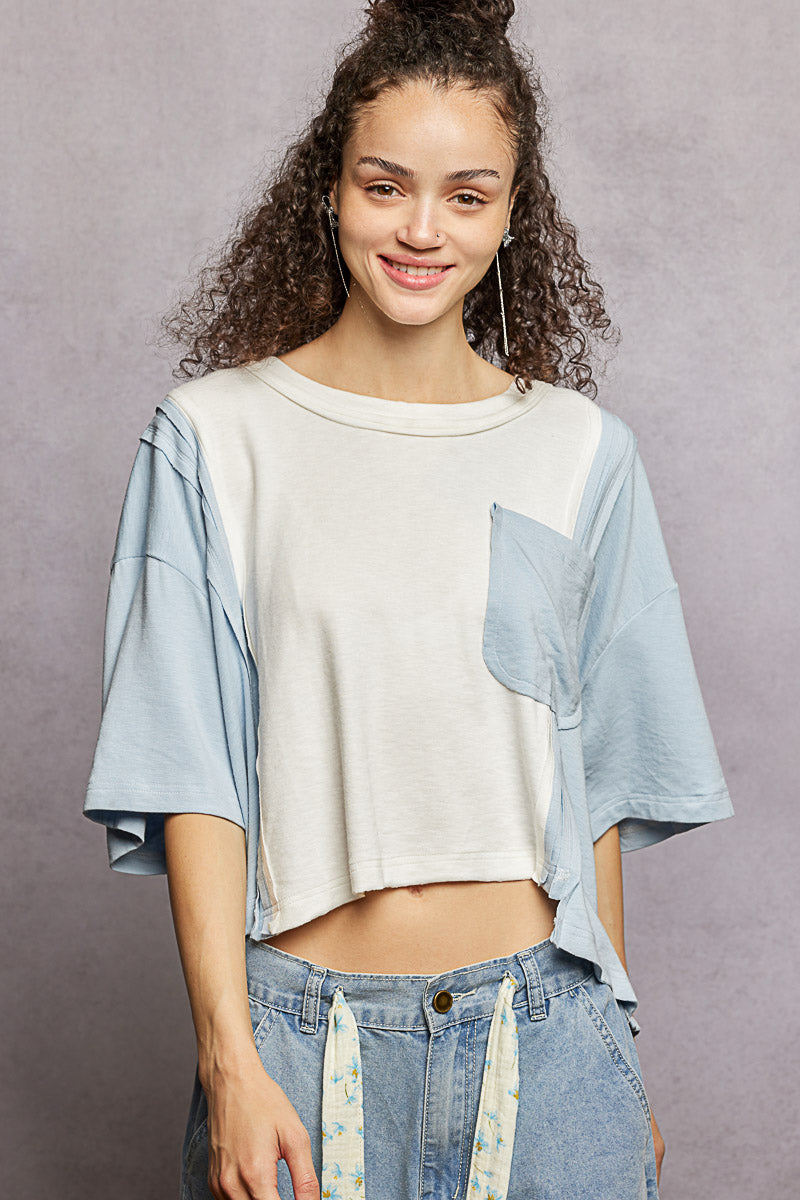 Woman wearing a light blue and white top with denim pants against a gray background