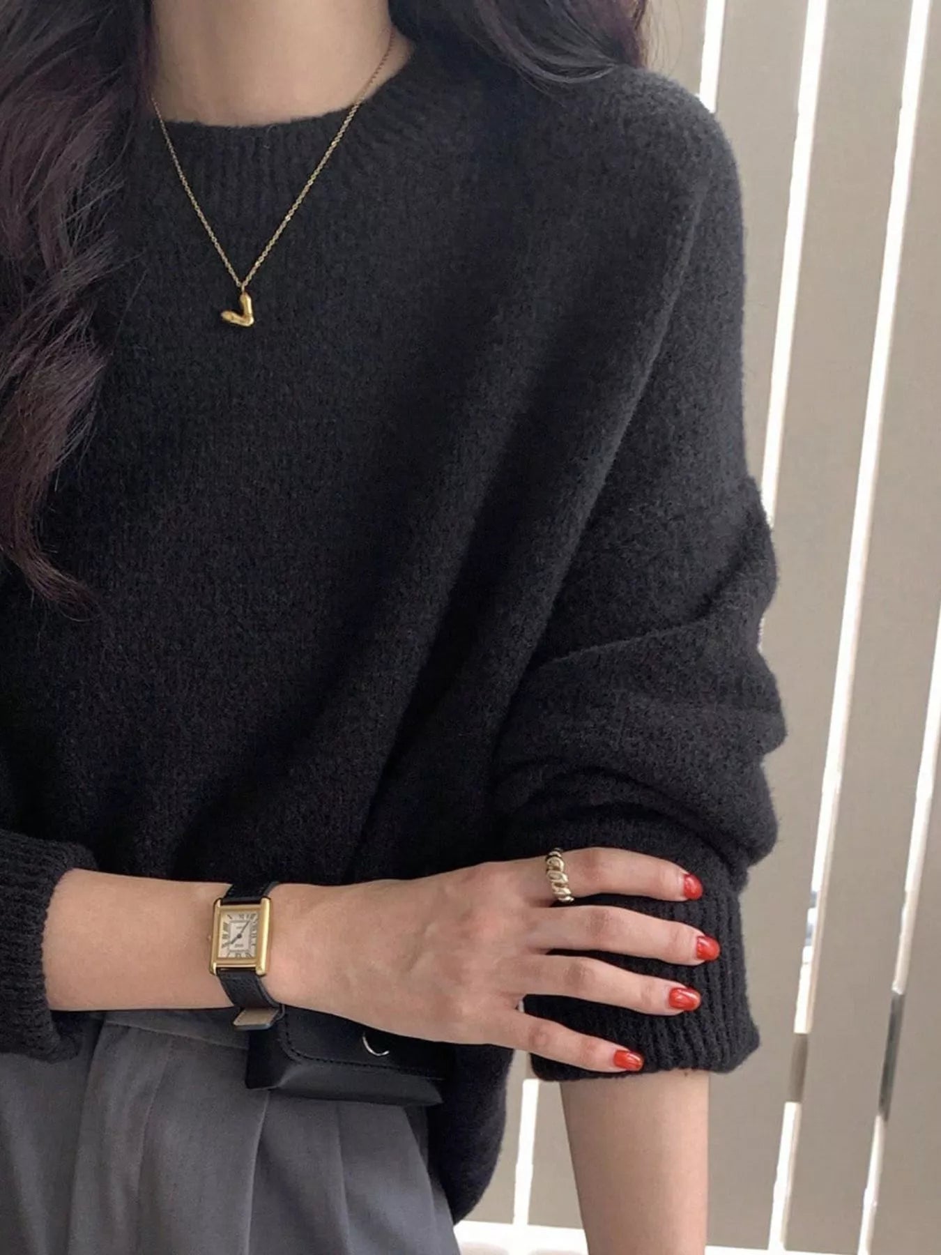 Person wearing a dark gray sweater with jewelry and red nail polish.