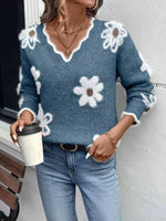 Person wearing a blue sweater with white floral patterns, holding a coffee cup.
