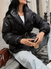 Person wearing a black puffer jacket sitting on a bench outdoors.