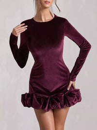 Purple velvet dress with long sleeves and ruffled skirt on a plain background