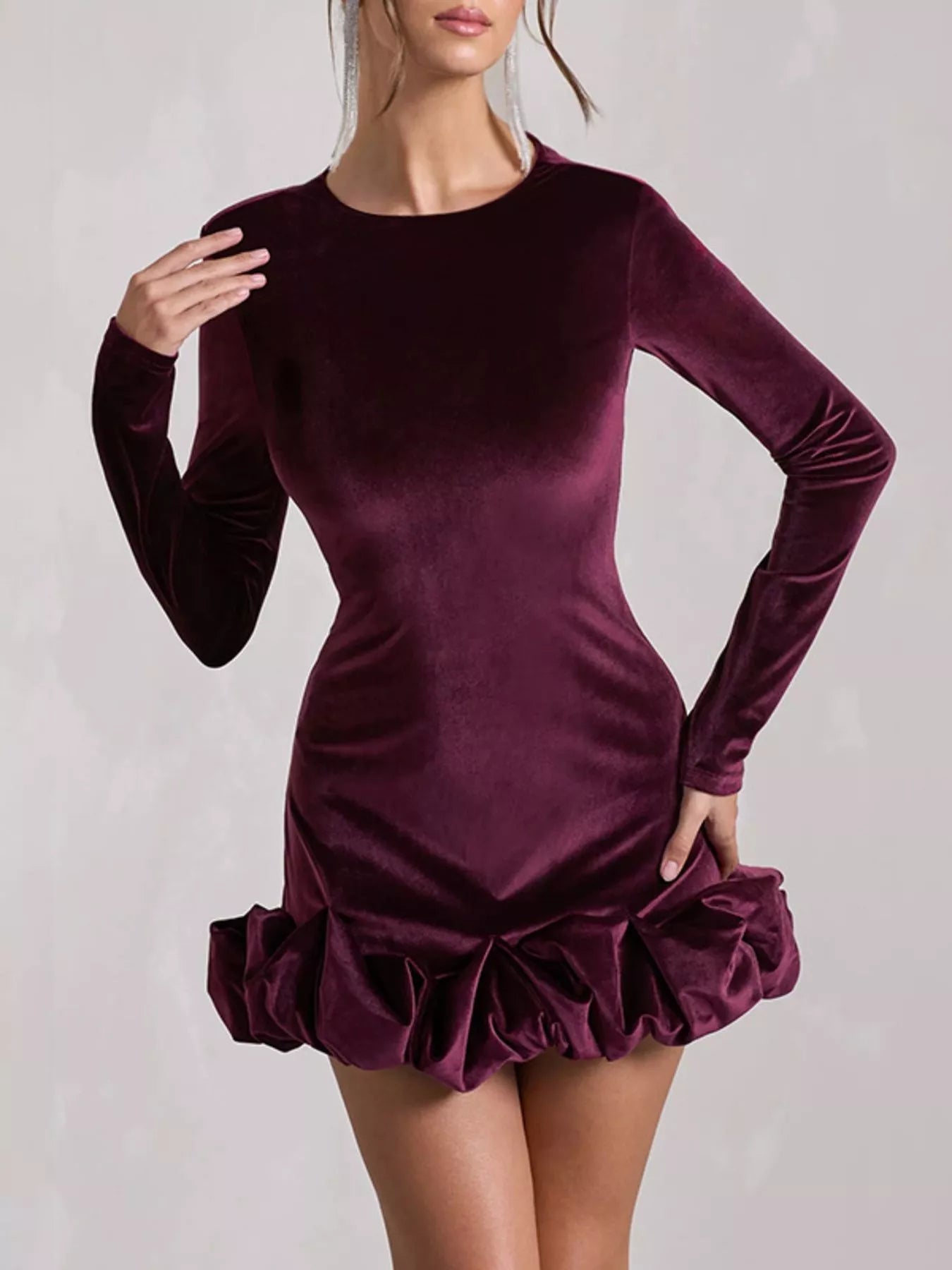 Purple velvet dress with long sleeves and ruffled skirt on a plain background
