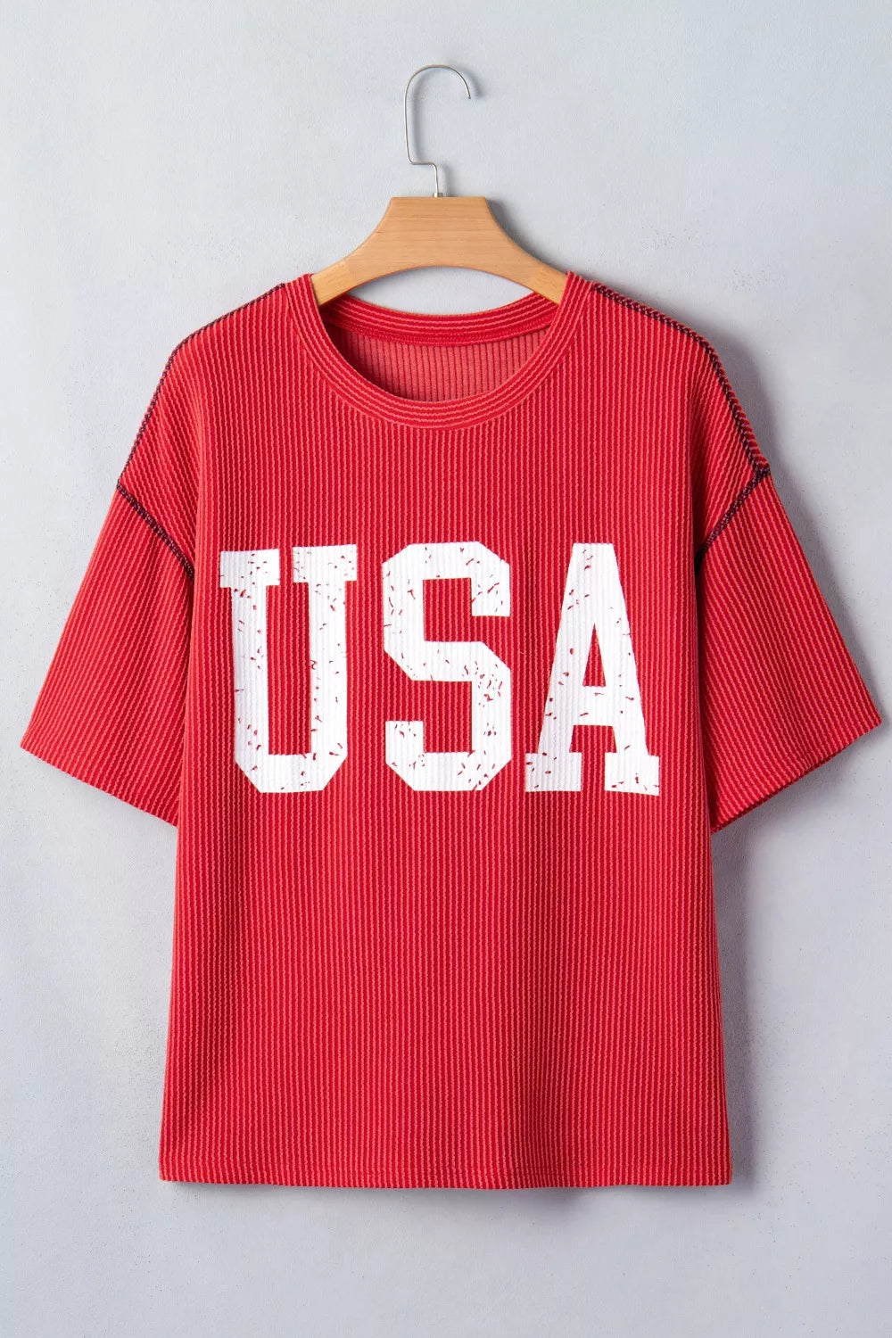 Red t-shirt with 'USA' print on a wooden hanger against a light gray background