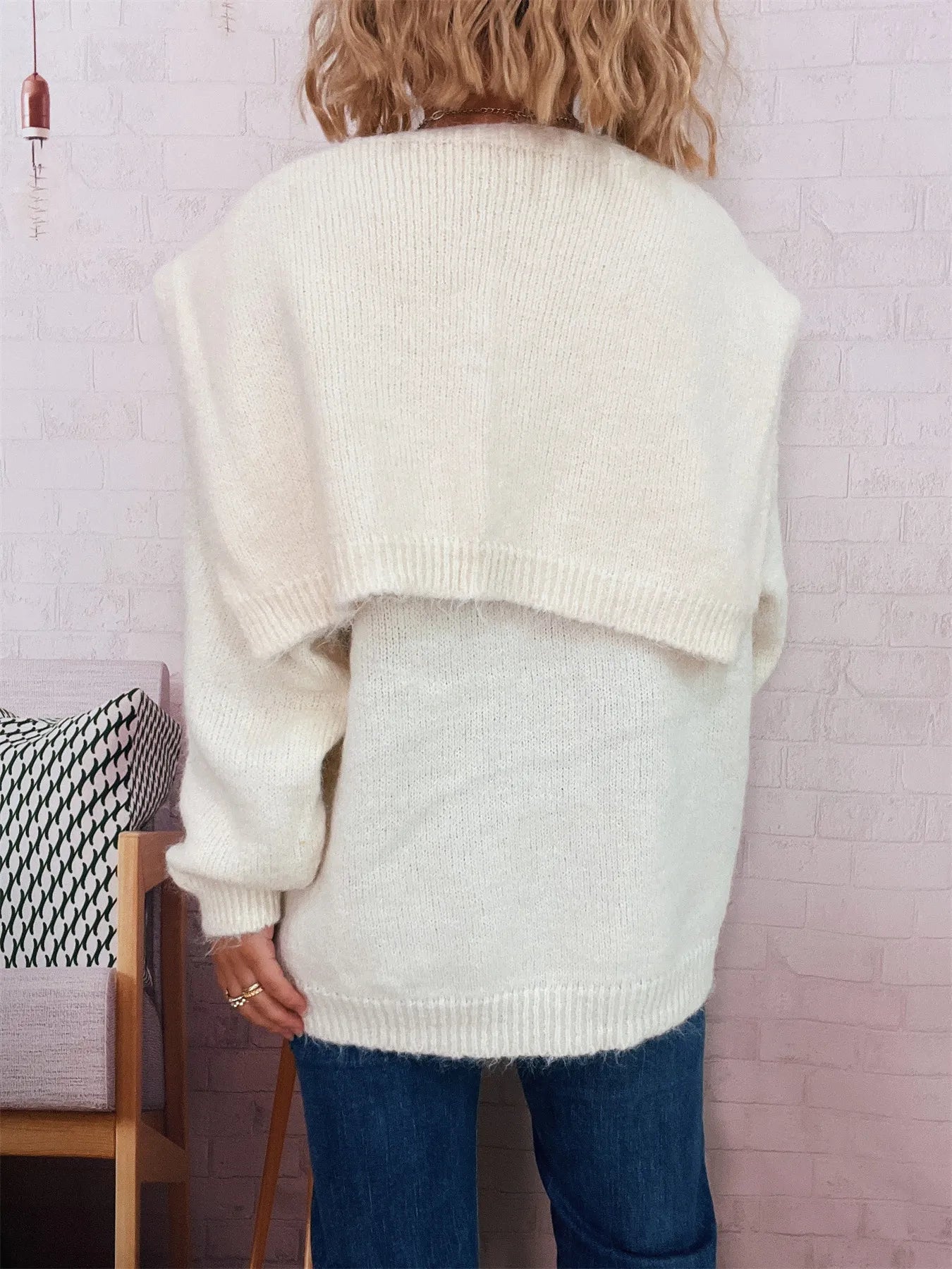 Person wearing a cream-colored sweater with a light green panel, standing against a white wall.