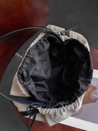 Close-up of a black bucket hat with beige interior on a wooden surface.