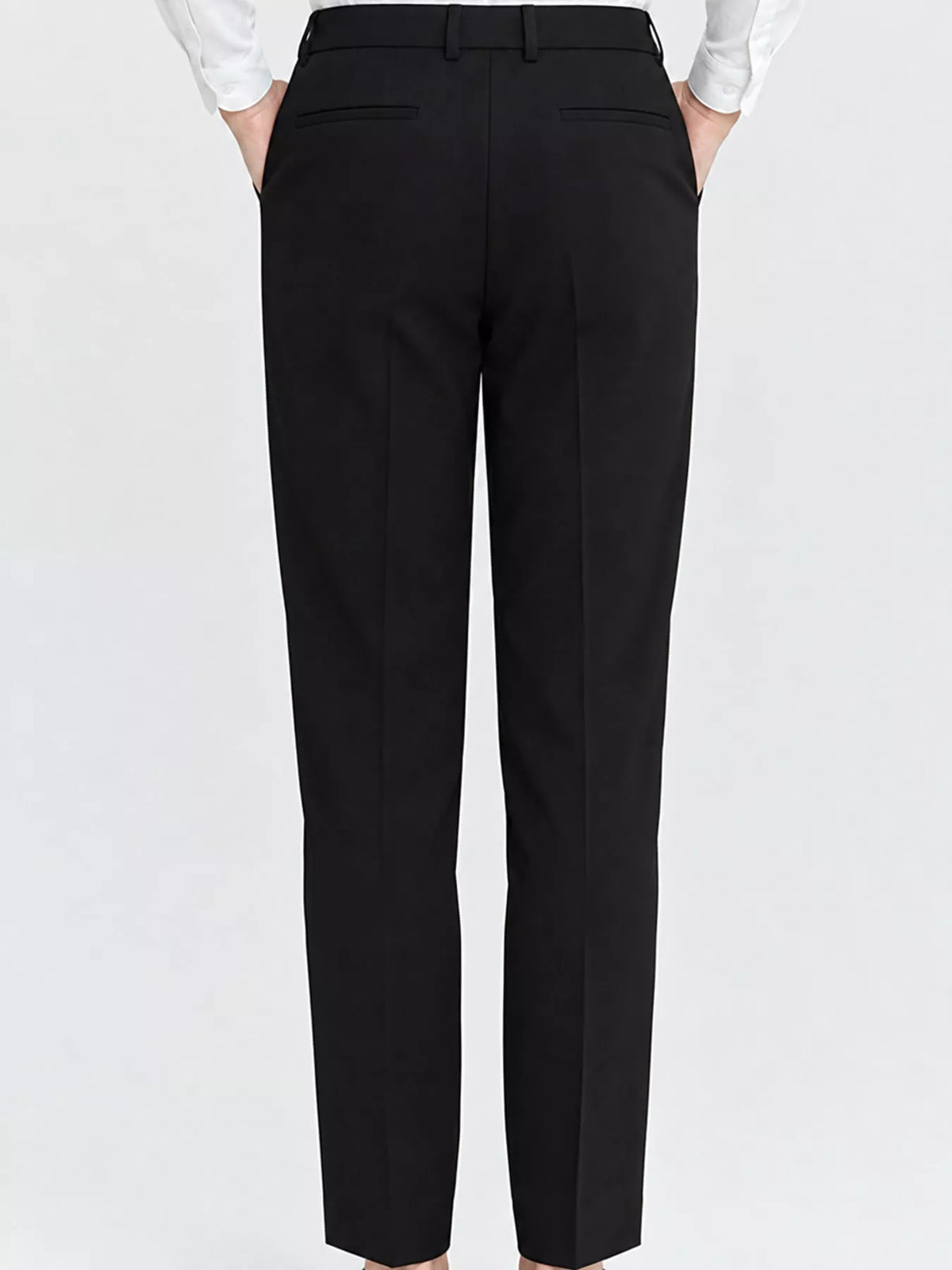 Black trousers shown from the back on a model, featuring a straight-leg fit, belt loops, and welt pockets, paired with a white long-sleeve shirt against a light gray background.