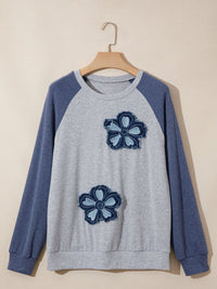 Gray sweatshirt with blue sleeves and flower patterns on a beige background