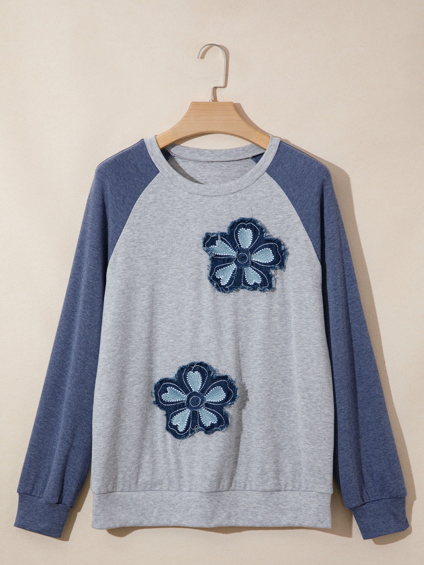Gray sweatshirt with blue sleeves and flower patterns on a beige background