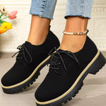 Black shoes with thick soles worn by a person, with a blurred background