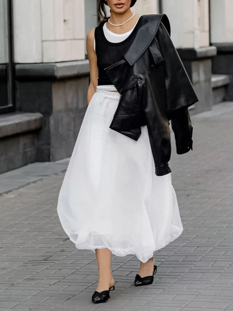 Person wearing a black leather jacket over a black top and white skirt on a city street.