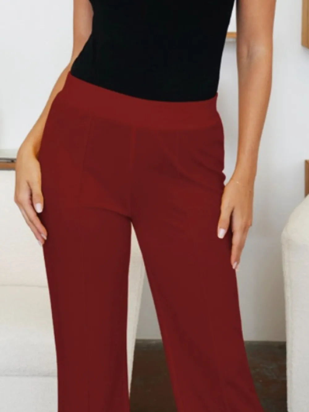 Person wearing red pants and a black top against a neutral background