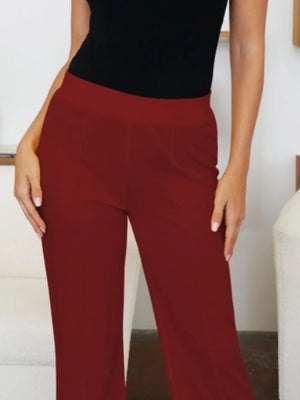 Person wearing red pants and a black top against a neutral background