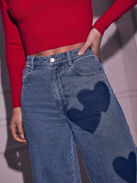 Person wearing blue jeans with heart patches and a red top.