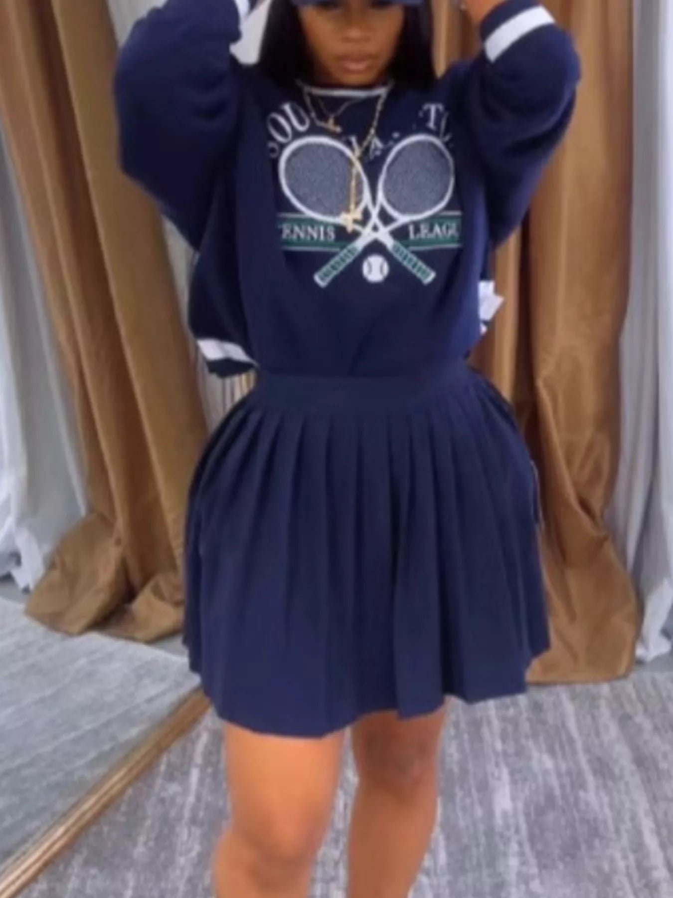 Person wearing a navy blue outfit with a tennis-themed design in front of a brown curtain.