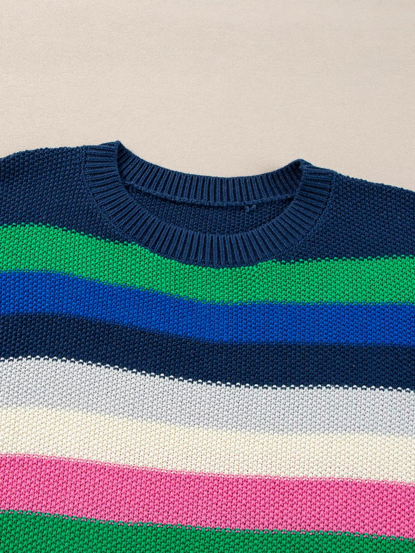 Colorful striped sweater with blue, green, pink, and white stripes on a beige background