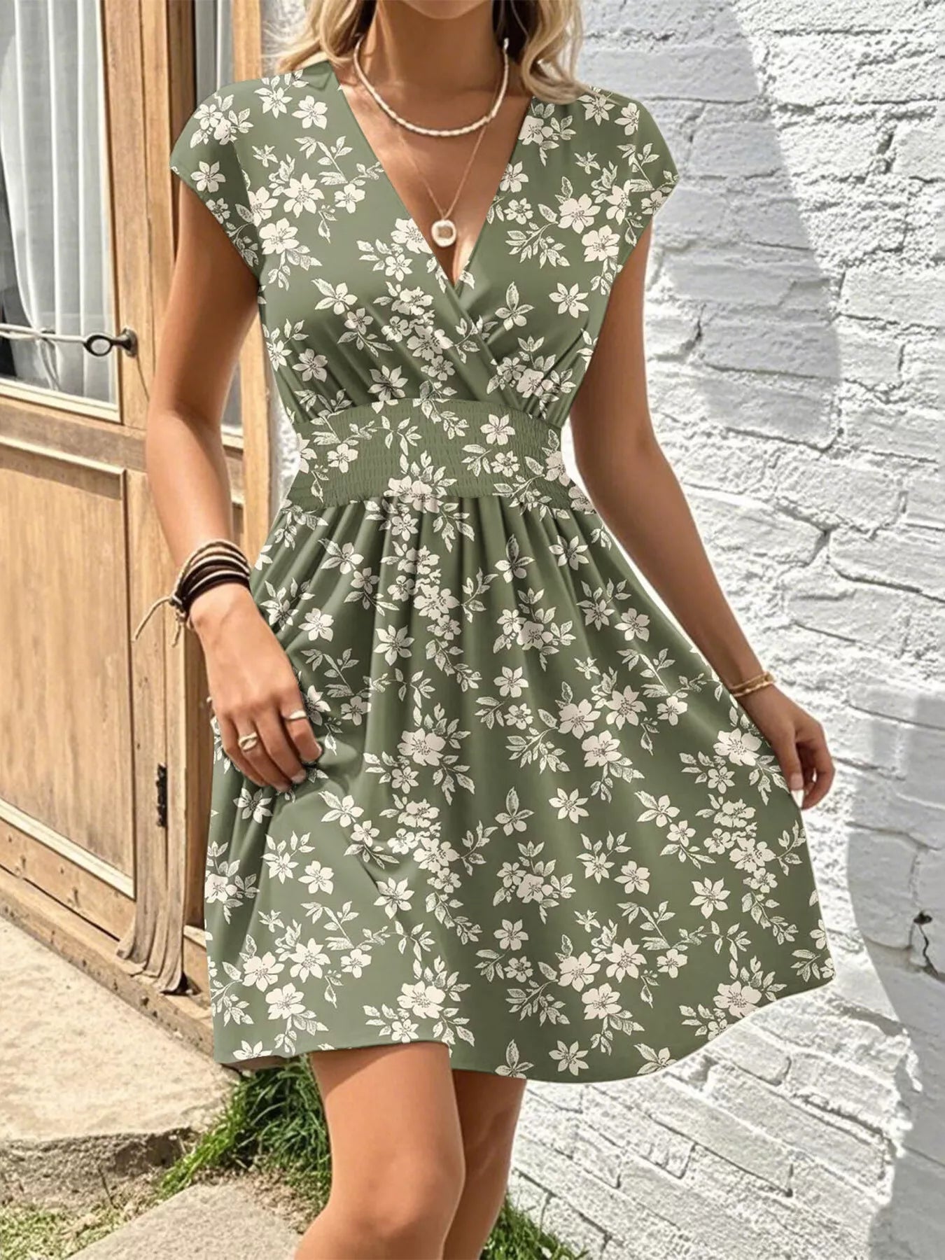 Woman wearing a green floral dress against a white brick wall.