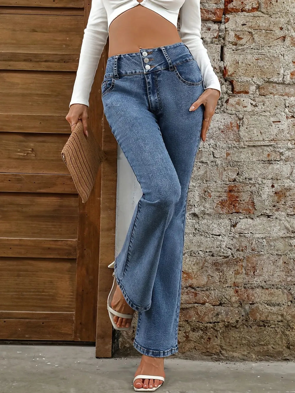 Person wearing high-waisted blue jeans and a white long-sleeve top against a brick wall.