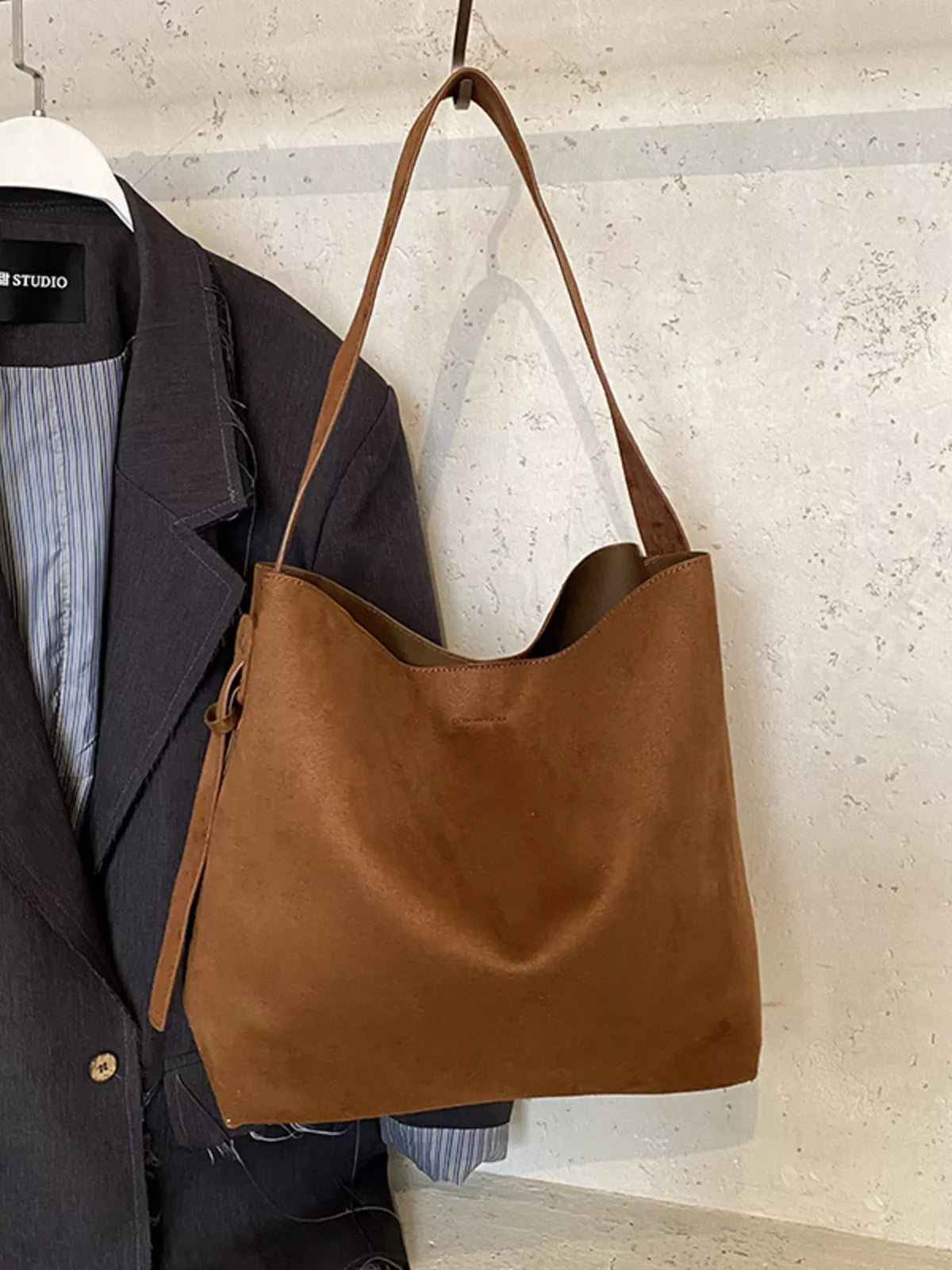 Brown leather handbag hanging on a coat rack with a neutral background