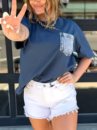 Person wearing a blue oversized shirt with a pocket design and white shorts, making a peace sign.