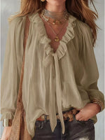 Woman wearing a light green blouse with ruffled details and layered necklaces.