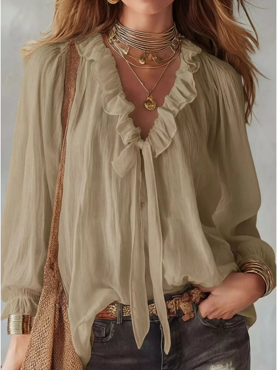 Woman wearing a light green blouse with ruffled details and layered necklaces.
