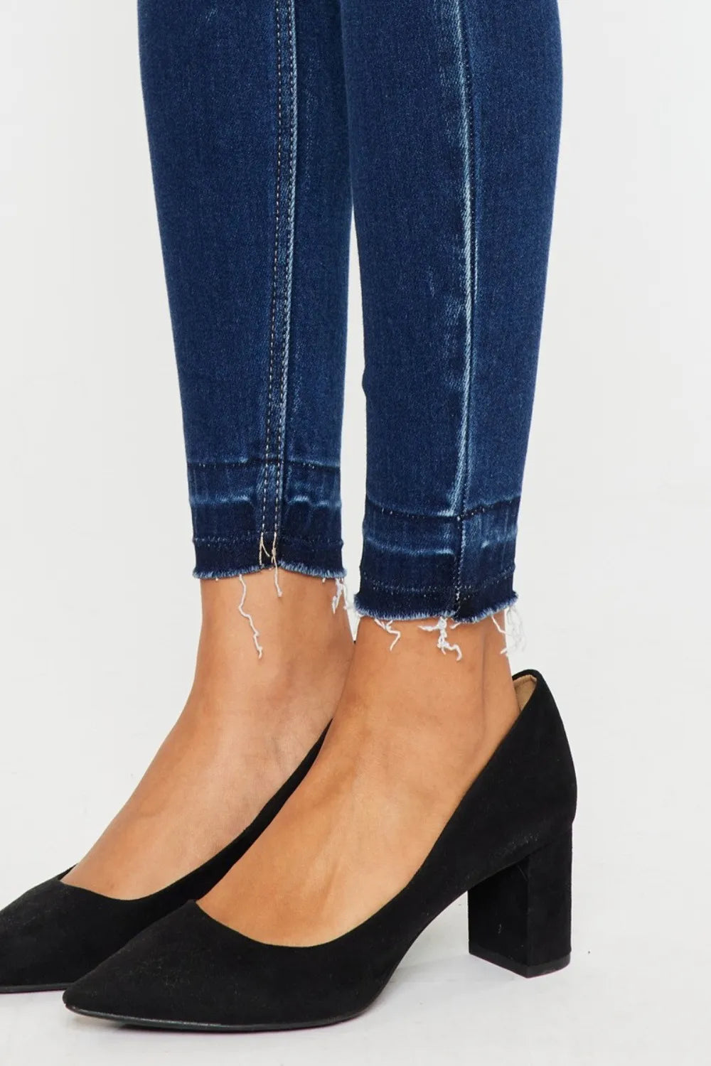 Black high-heeled shoes worn with blue jeans on a white background