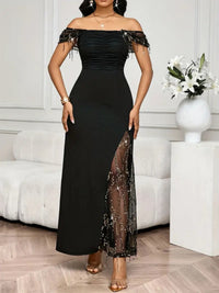Woman wearing a black off-shoulder dress with sheer panels in a room.