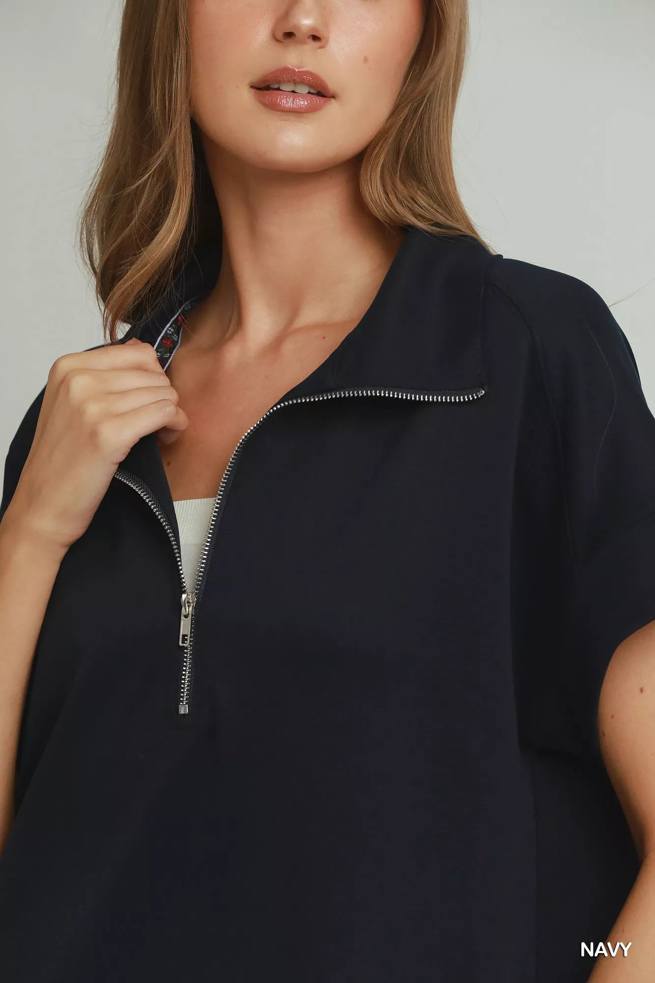 Woman wearing a navy blue zip-up top against a neutral background