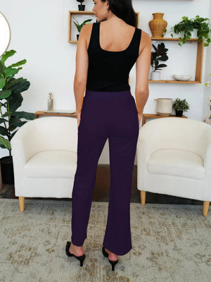 Woman wearing a black tank top and purple pants standing in a living room.