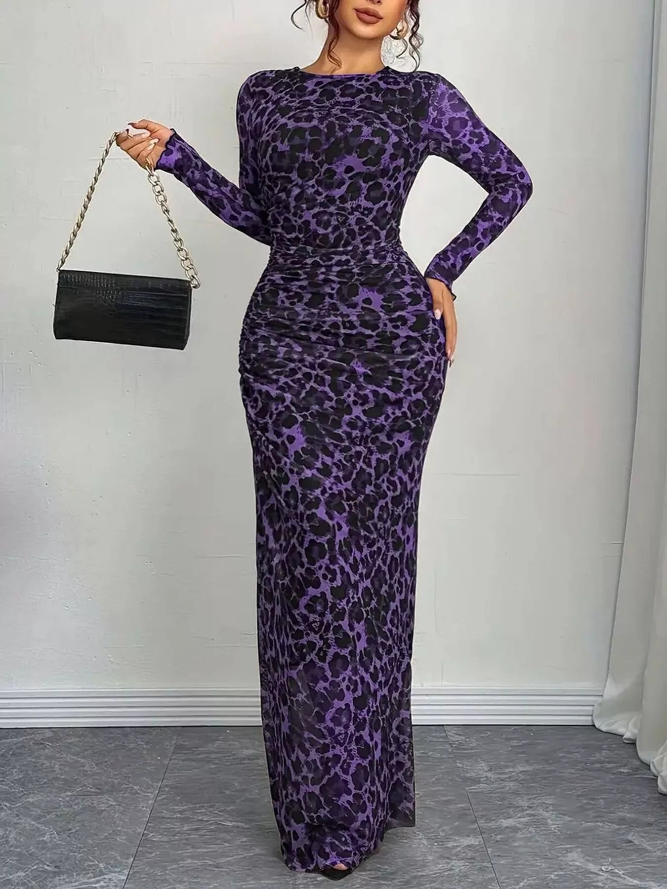 Woman wearing a purple leopard print dress holding a black handbag against a white background