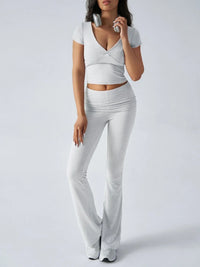 Woman wearing a white outfit with a deep neckline and flared pants on a plain background