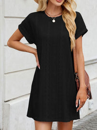 Woman wearing a black dress standing against a light-colored wall.