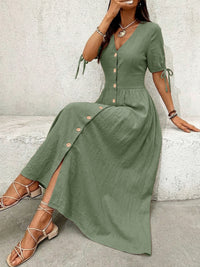 Woman wearing a green dress with buttons sitting against a light gray wall.