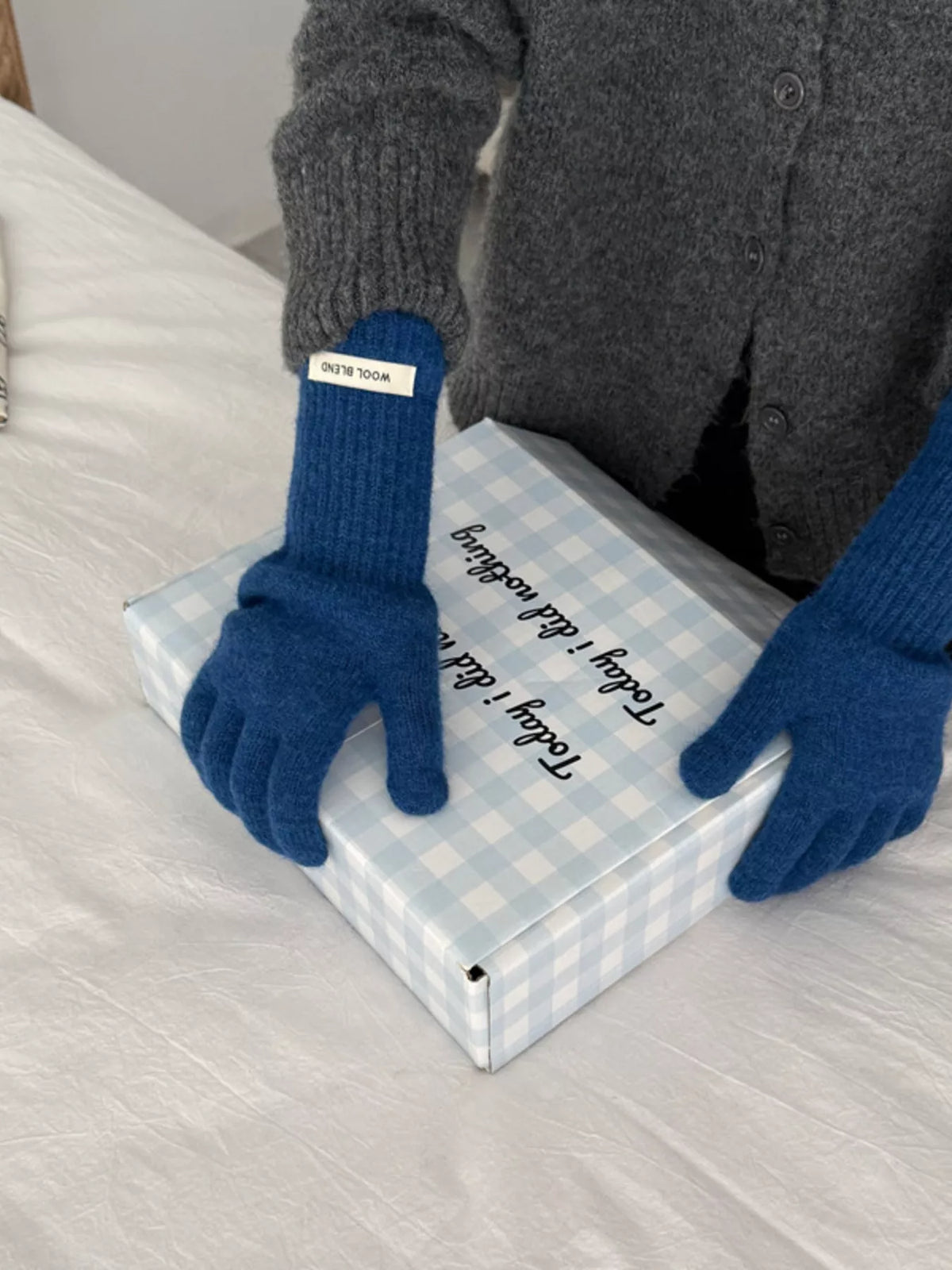 Person wearing blue gloves holding a wrapped gift box on a bed