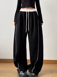 Person wearing black pants with white drawstring and trim on a plain background