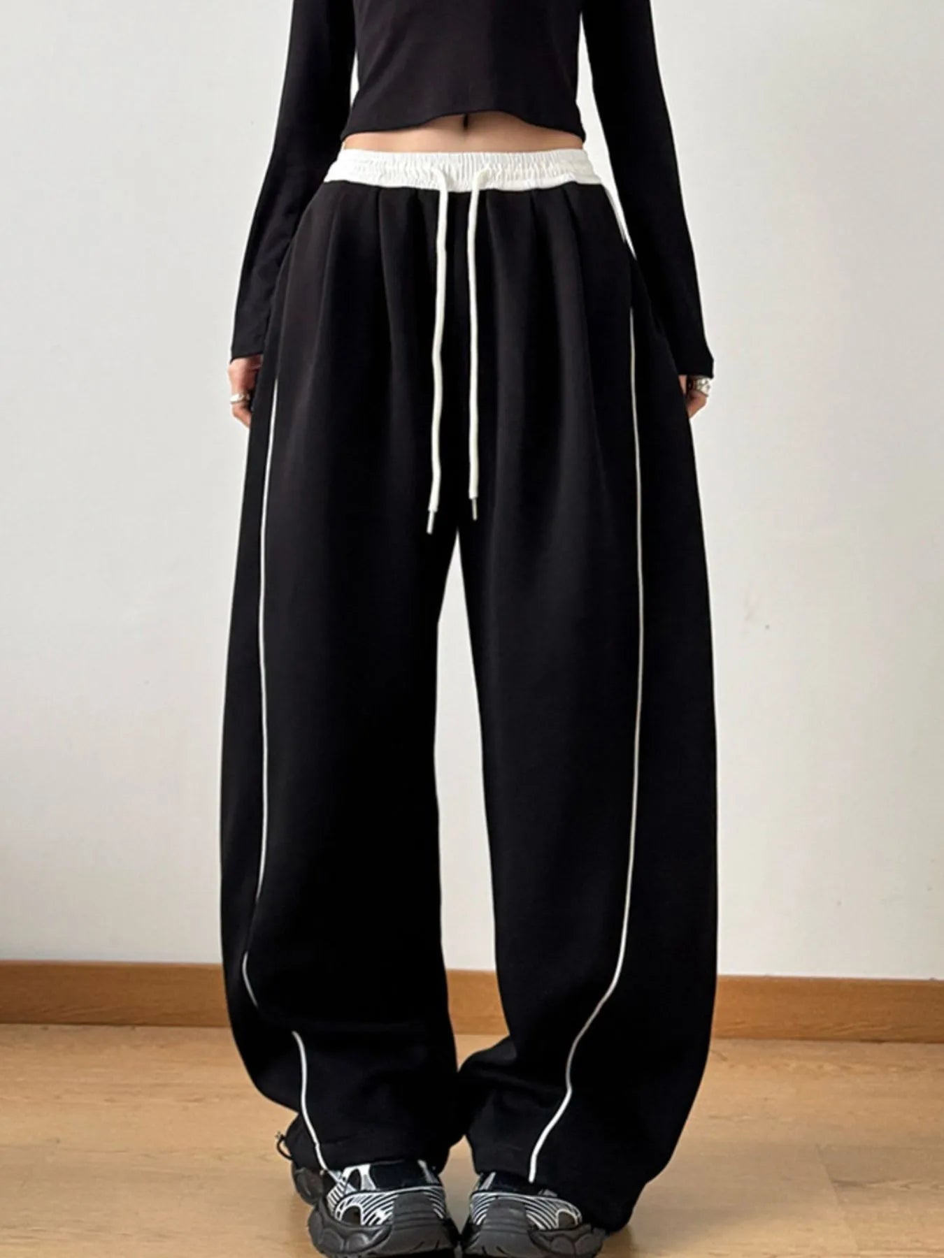 Person wearing black pants with white drawstring and trim on a plain background