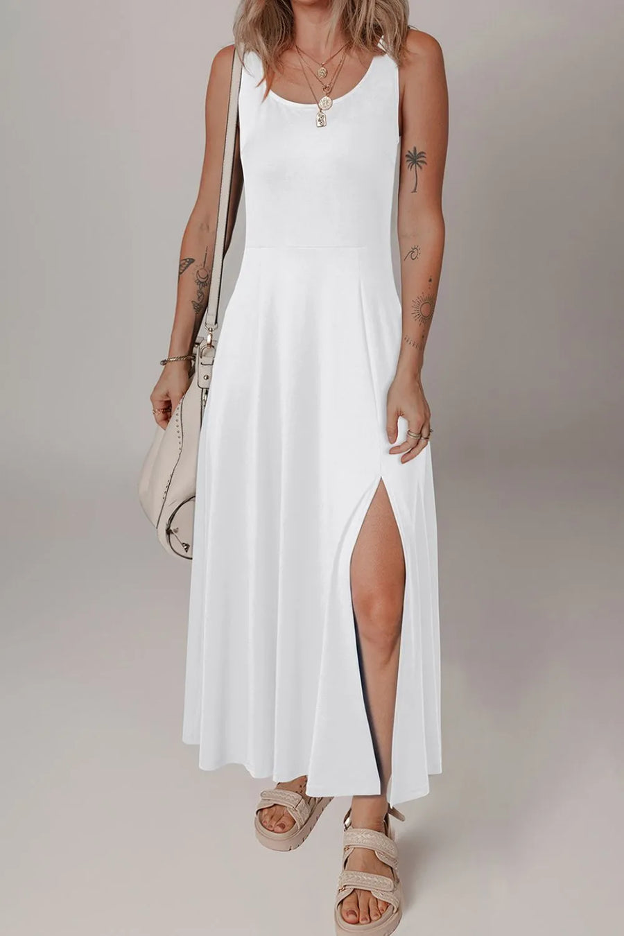 Woman wearing a white sleeveless dress with a slit on a plain background