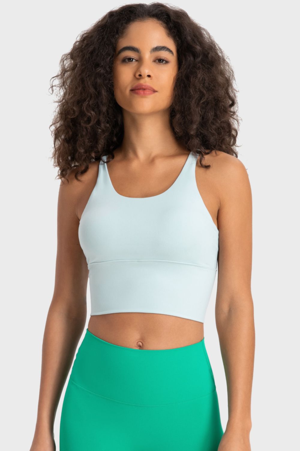 Woman wearing a light blue sports bra and green leggings on a white background