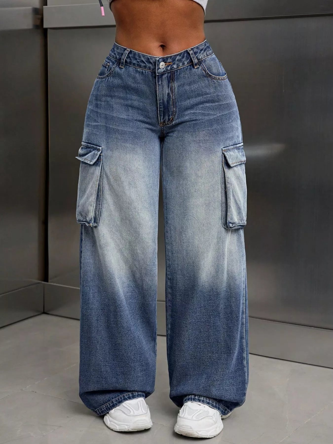 Wide-leg blue jeans with cargo pockets worn by a person on a neutral background