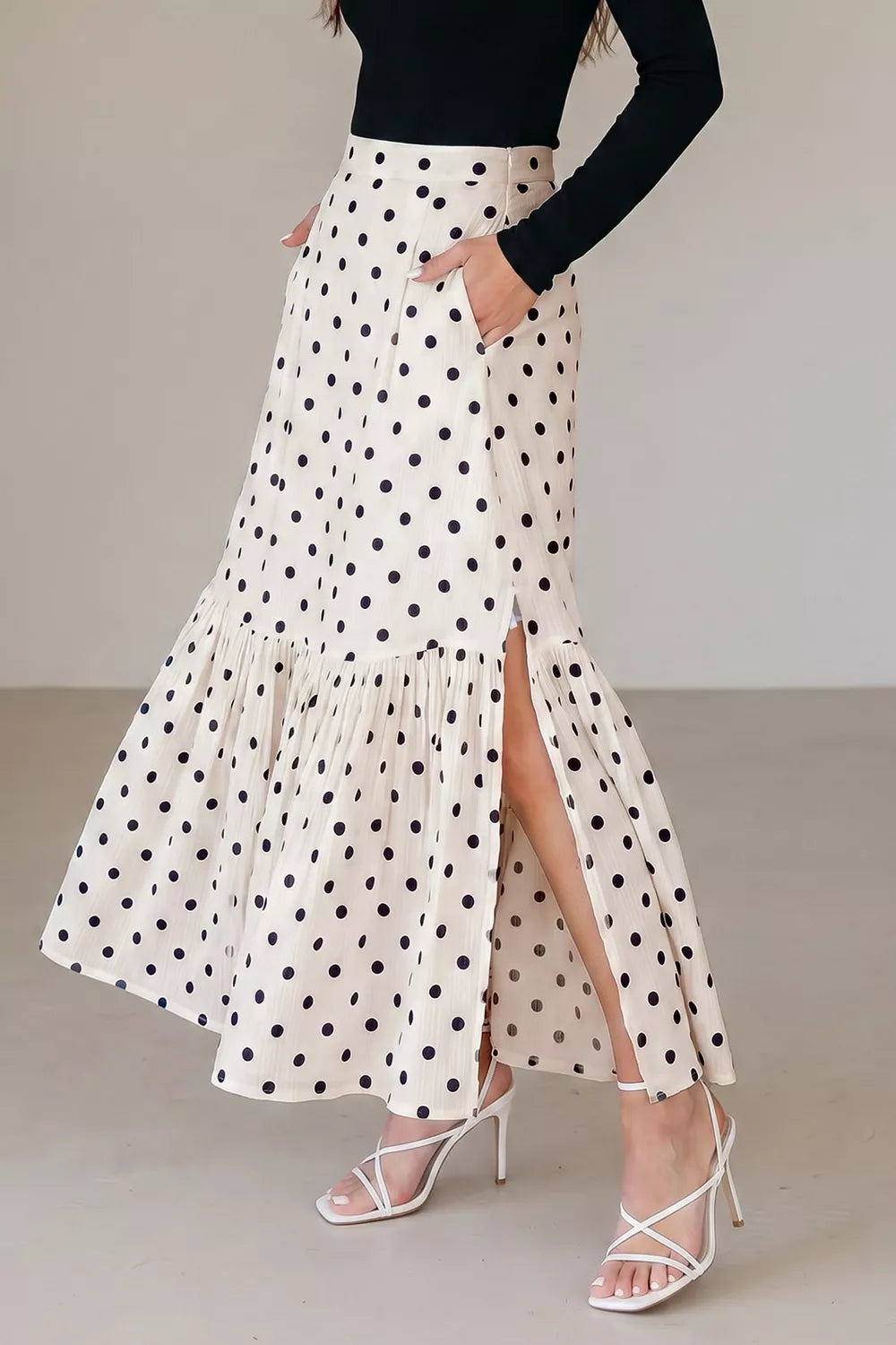 Woman wearing a polka dot skirt with a high slit on a plain background