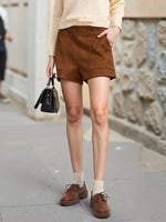 Person wearing brown shorts and shoes, holding a black handbag on a street.