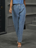 Person wearing blue jeans with pearl embellishments in an urban setting.