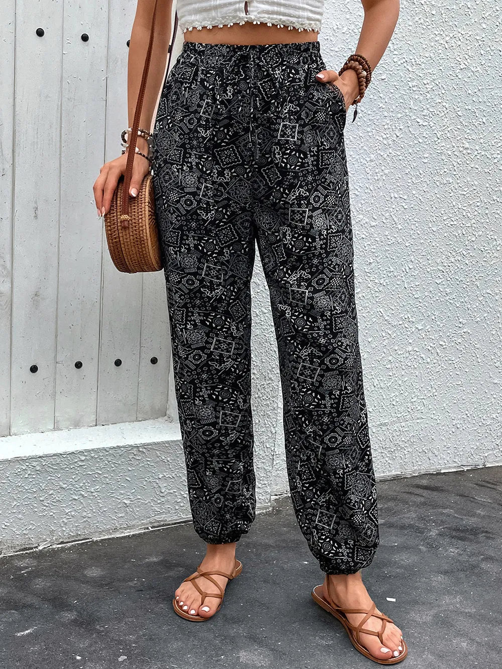 Person wearing black patterned pants standing against a light gray wall.