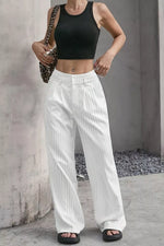 A model wearing white pinstriped wide-leg pants and a black crop top, standing against a concrete wall.