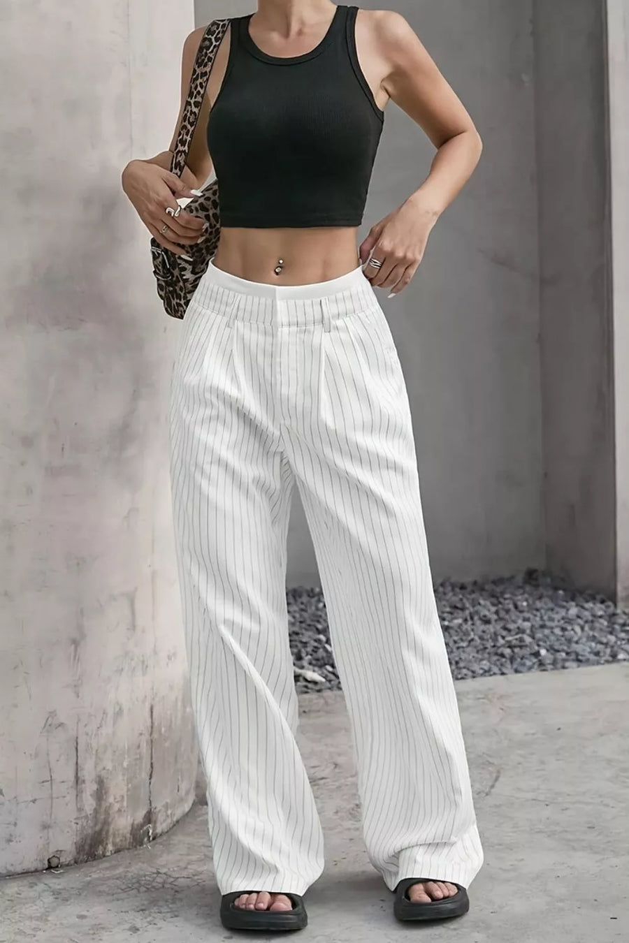 A model wearing white pinstriped wide-leg pants and a black crop top, standing against a concrete wall.