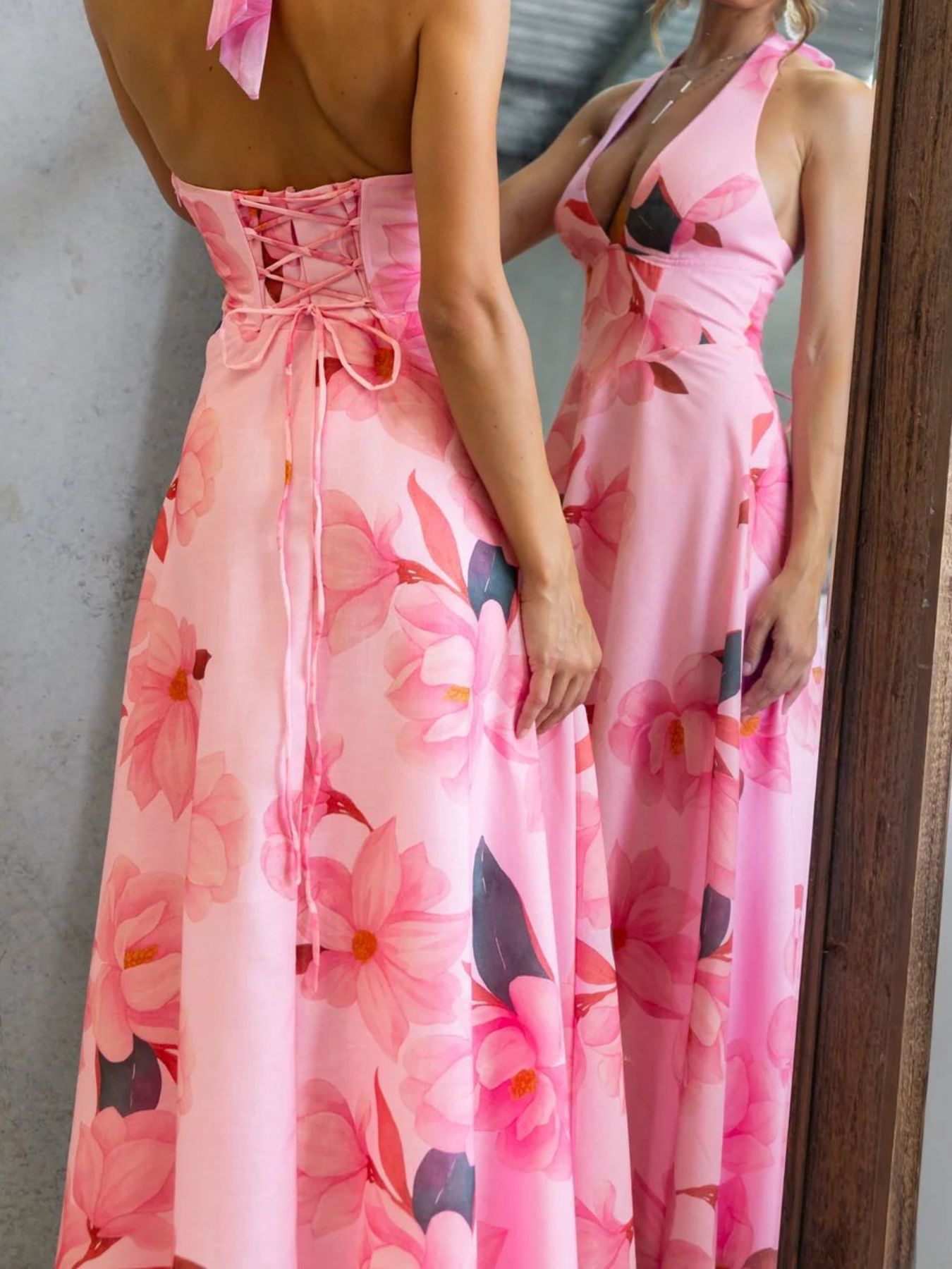 Woman wearing a pink floral dress standing in front of a mirror.