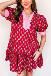 Woman wearing a red floral dress with pink trim against a white background