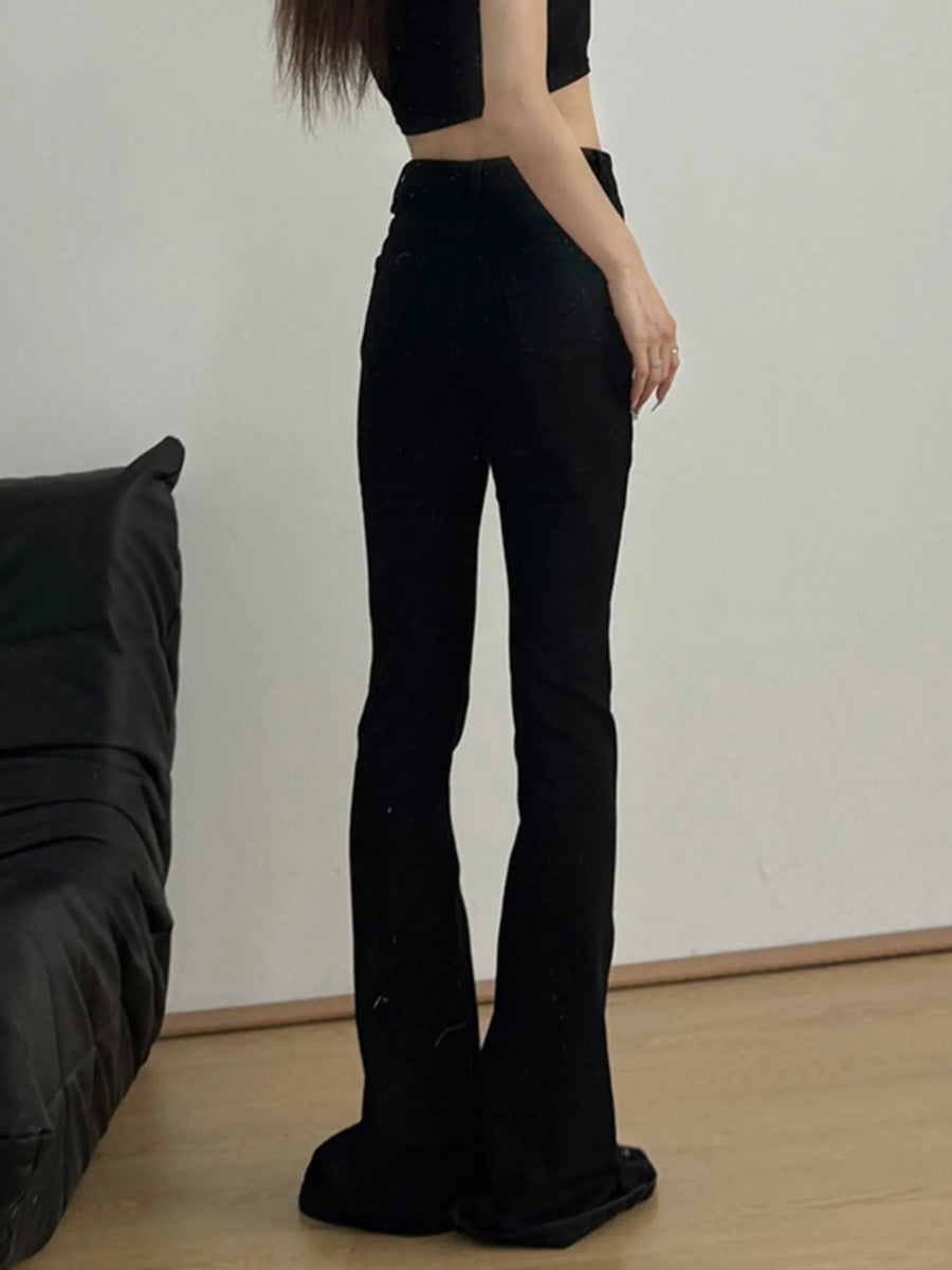 Person wearing black flared pants standing against a plain wall.