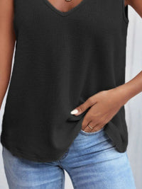 Person wearing a black sleeveless top and blue jeans on a plain background