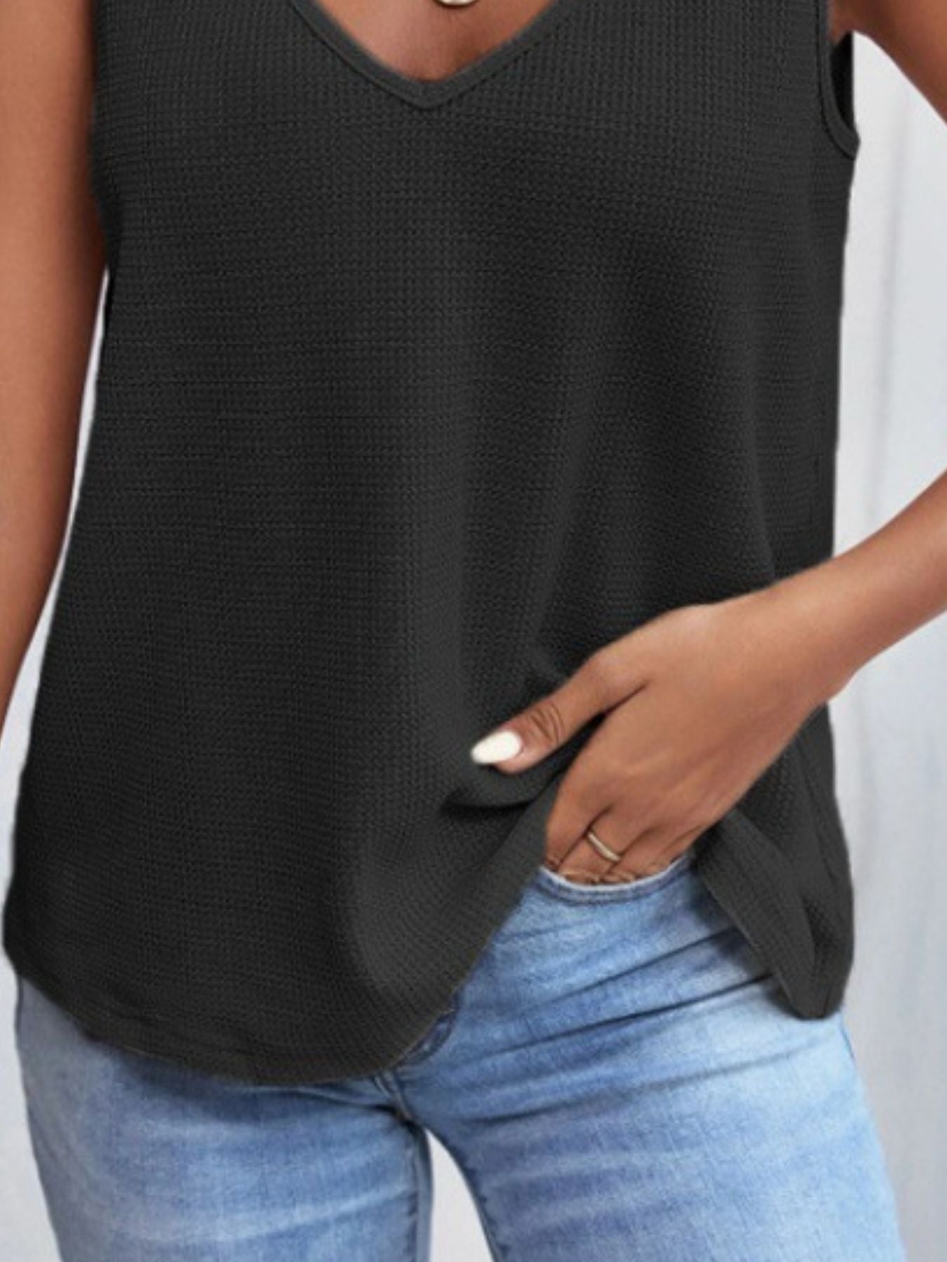 Person wearing a black sleeveless top and blue jeans on a plain background